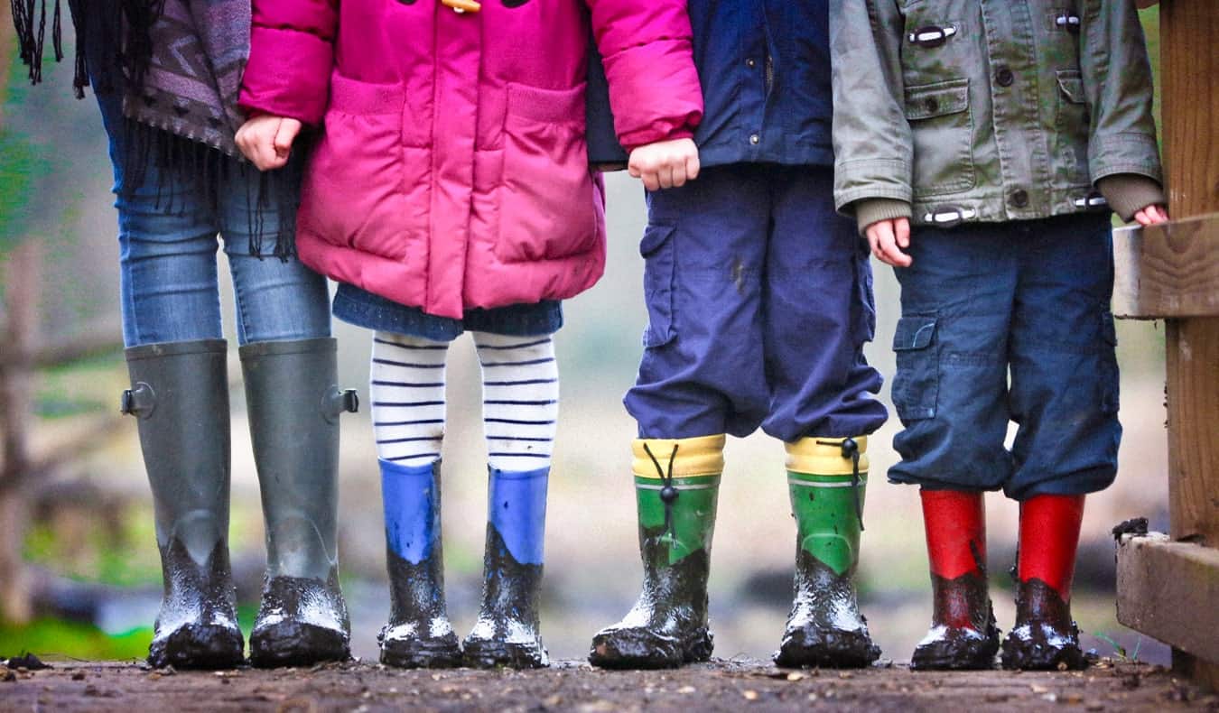An au pair standing with kids wearing rain boots in the mud